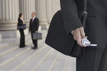 An image of two attorneys talking on the courthous steps and a third person checking their mobile phone.