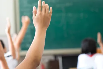 Students in a classroom with hands raised.